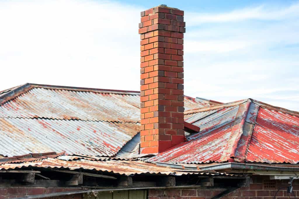 A tall brick chimney and worn out rusted metal roofing
