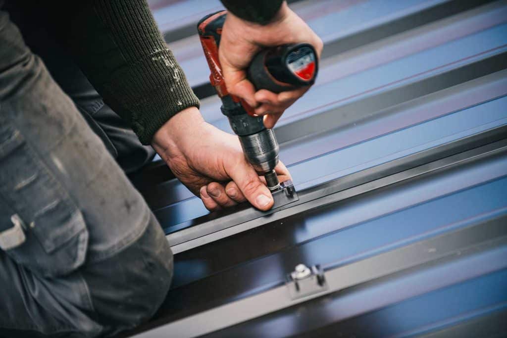 Building contractor is installing metal roofing sheets on the rooftop of the house using electric screwdriver