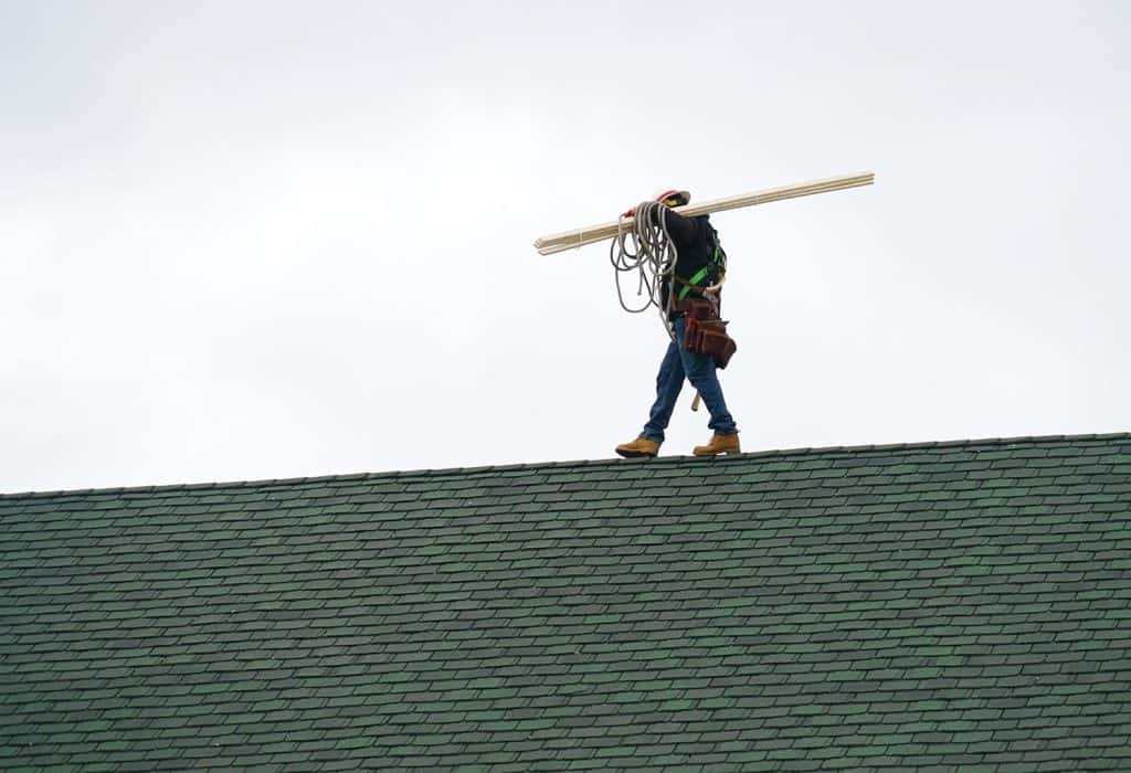 Manual roof repair worker walking on the roof carrying lumber wood