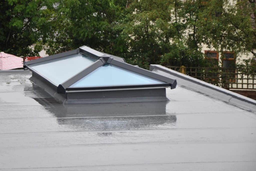Modern glass roof lantern or light on contemporary grey flat roof in the rain 