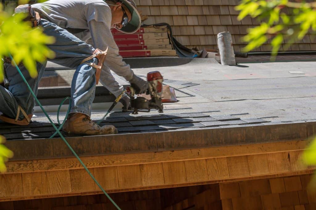 Roofer using a nail gun to install a roof shingle tab