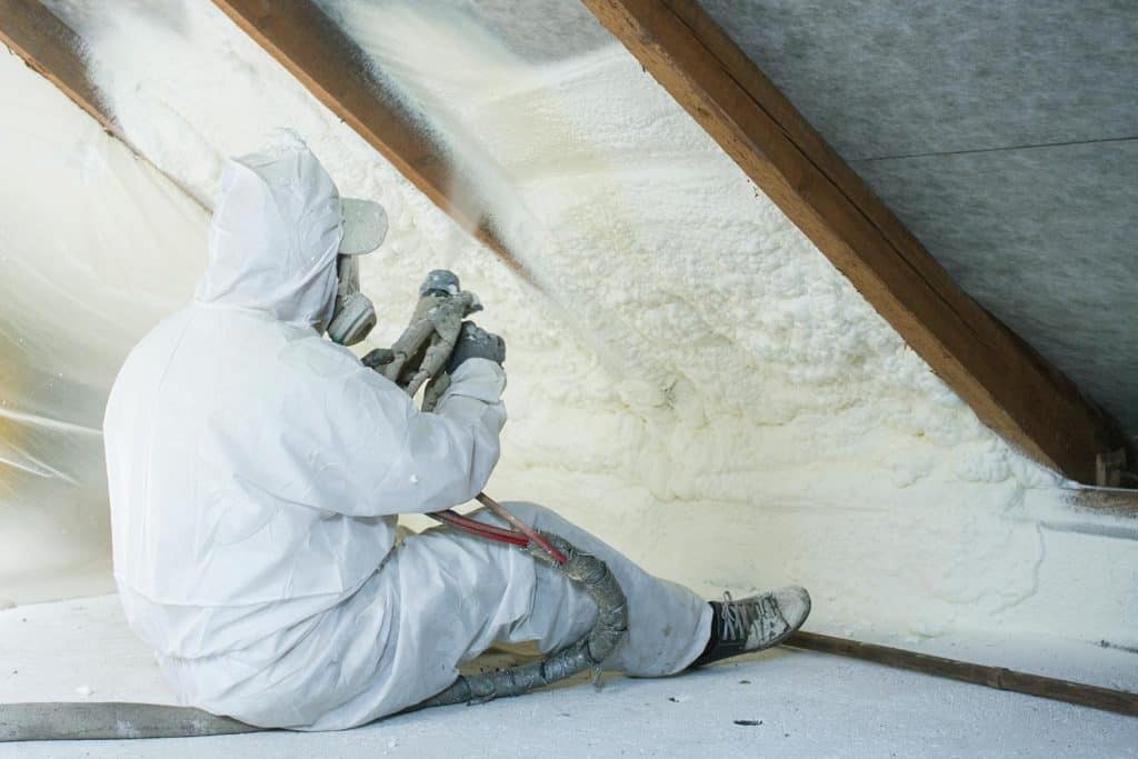Technician spraying foam insulation using plural component gun for polyurethane foam