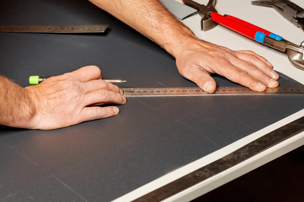 The male hands of a worker marks out a sheet of roofing iron with a pencil and a ruler