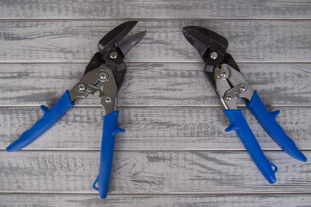 Two tin snips or metal scissors on a grey wooden background