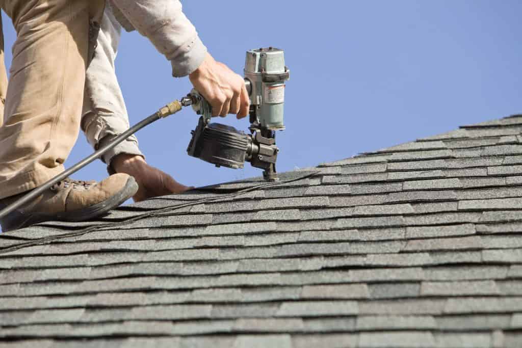 Worker using a nail gun to install the new gray asphalt shingle roofing