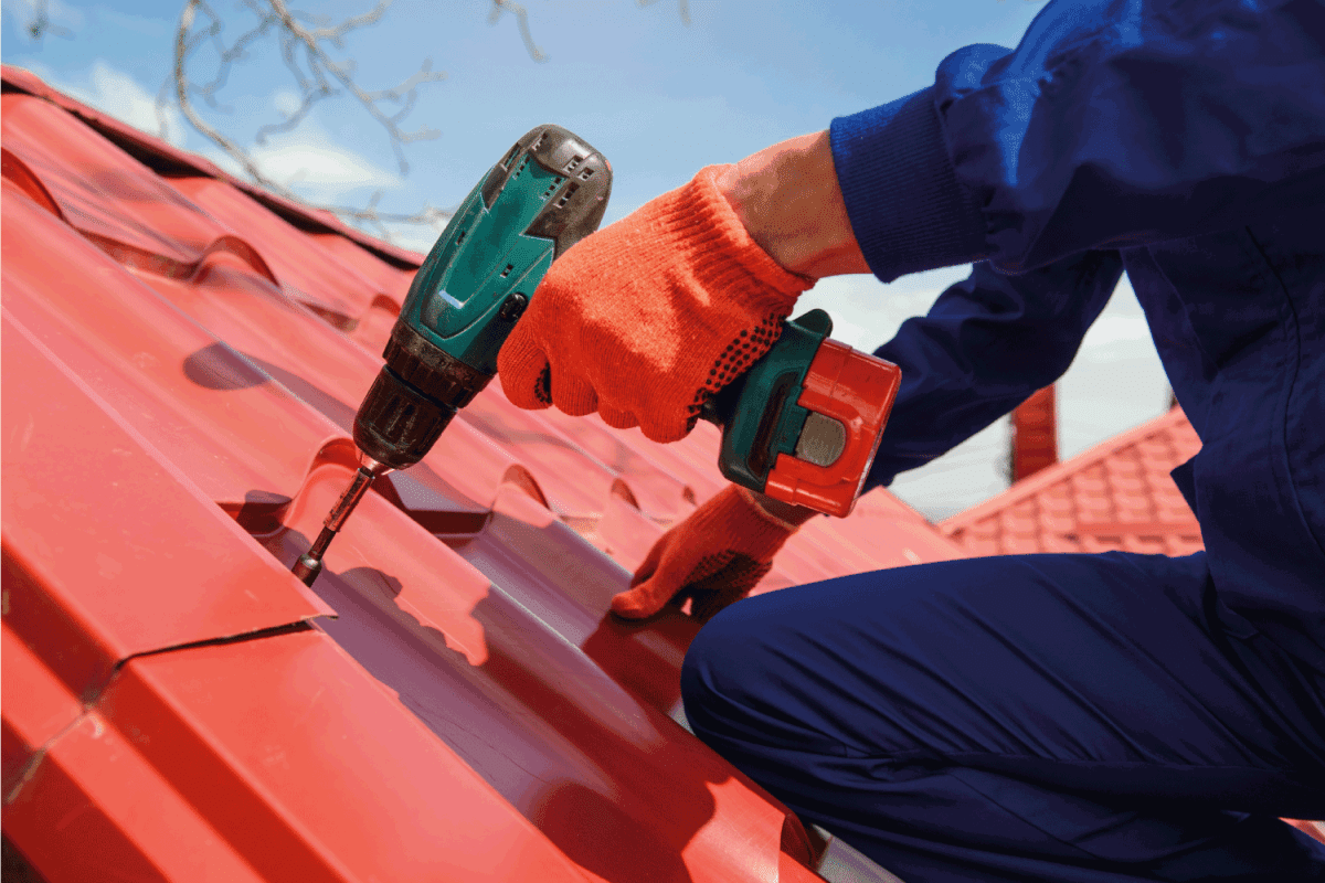 hands in protective gloves of young man worker who fix a metal tile roof with screwdriver. Roofing work