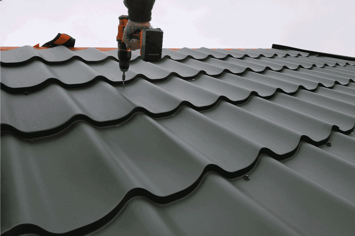 professional worker works on installation of a roof of a roof by sheets of a metal tile and drills a screw