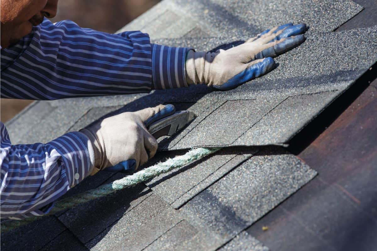 roofer worker cutting asphalt shingles to fit for installation using cutter