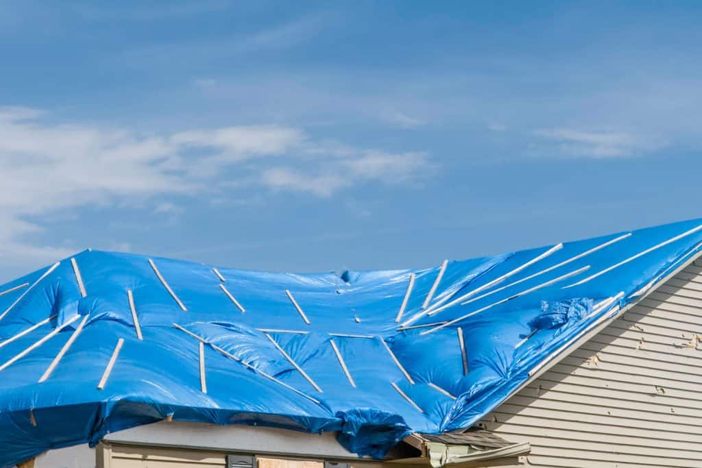 A blue colored tarp laid on the roof of a two story house