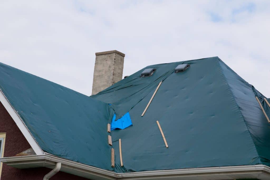 A dark green colored tarp on the roof of a huge house