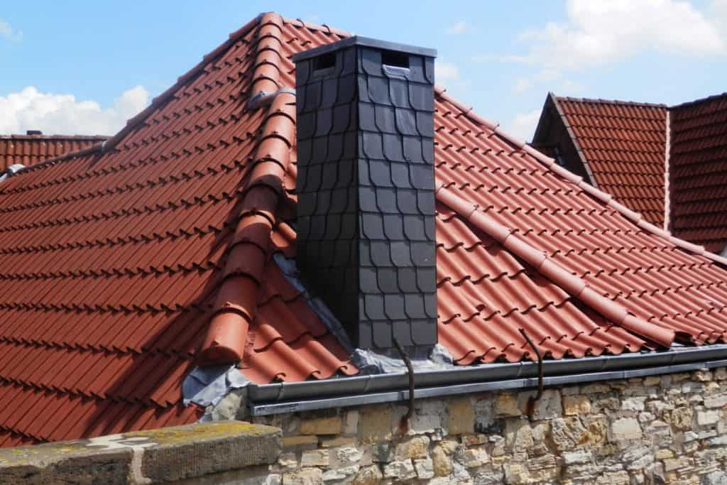 A high pitch roof with metal roofing and a chimney with decorative stone cladding