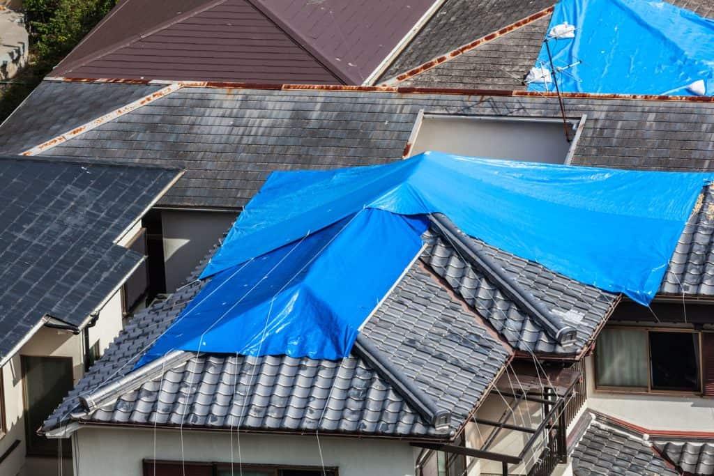 A house under construction with blue tarp laid over on top of the roof