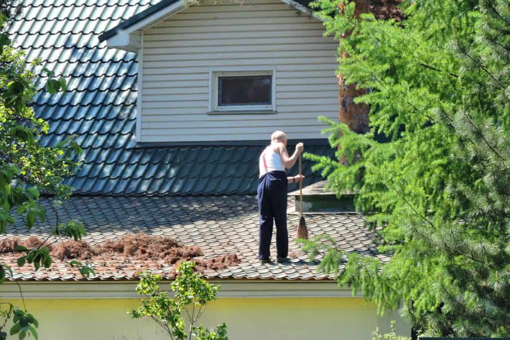 A man with a broom cleans sweeps roof in a country house