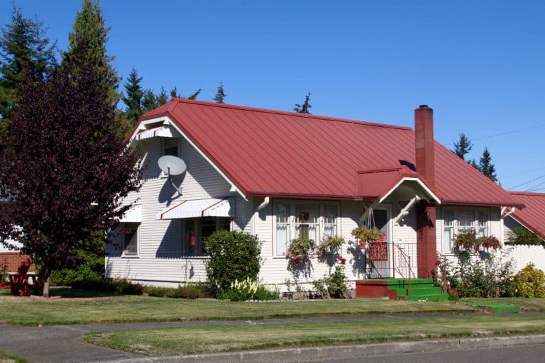A remodeled old house painted in white and matched with red roofing along with pine trees on the side, What Are The Different Types of Metal Roof Trims?