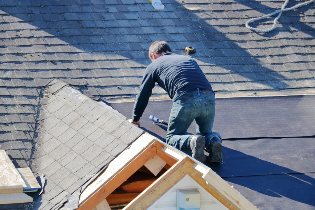 A roofer uses a nail gun to apply tarp to a roof in preparations for shingling.

