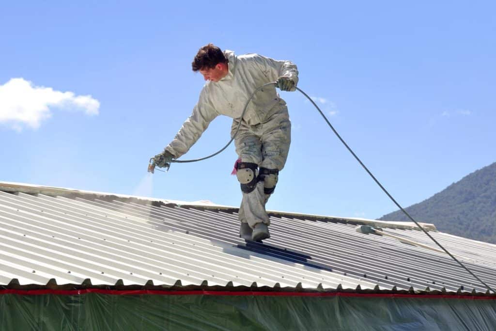 A trademan uses an airless spray to paint the roof of a building