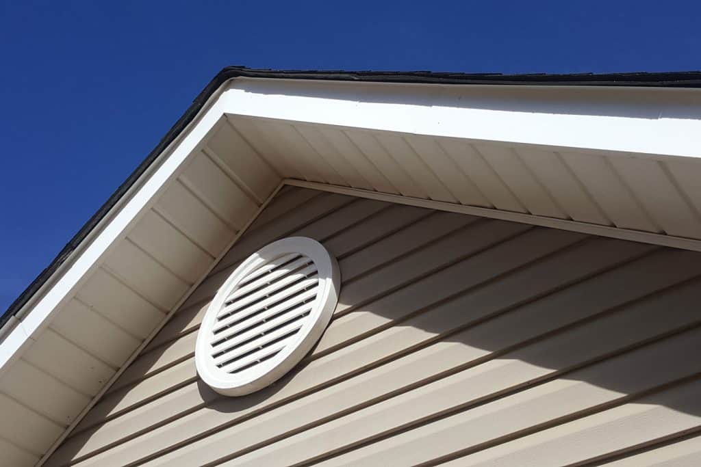 A white round exhaust vent on the attic of a house