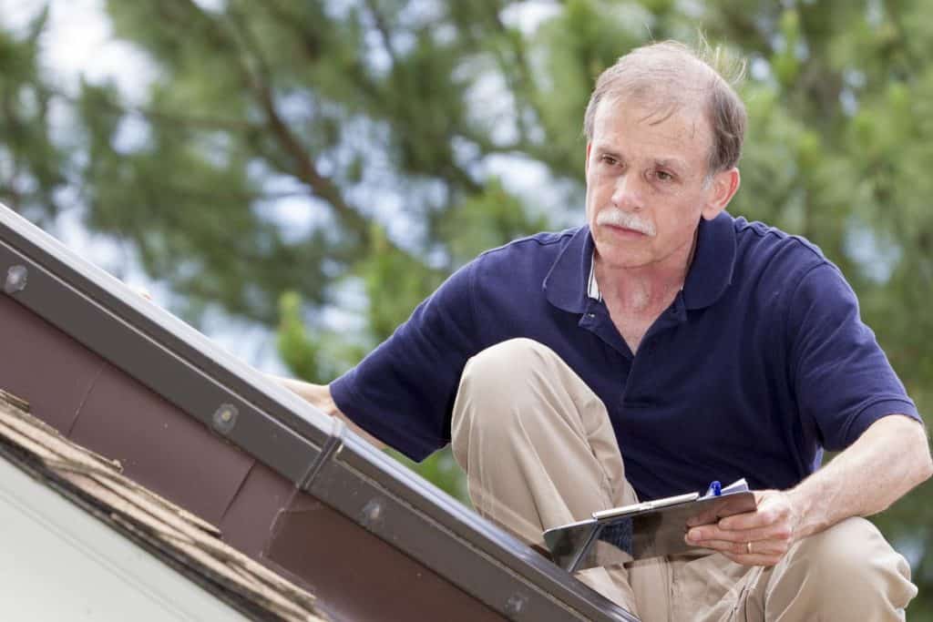 An inspector on the roof of a residential structure examines a skylight