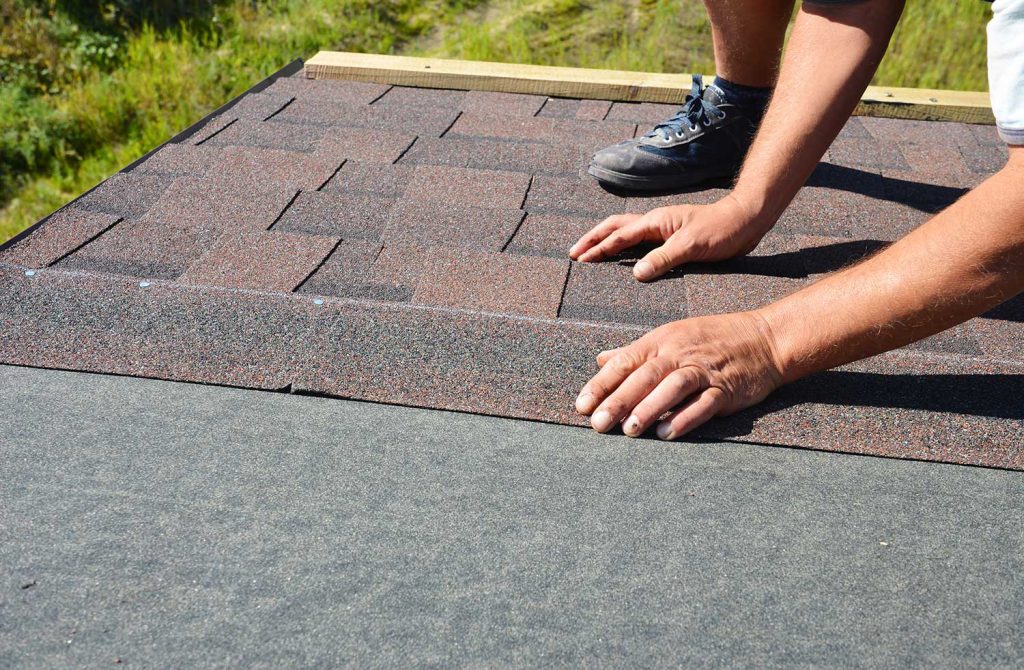 Building contractor installing dimensional asphalt roof shingles on rooftop