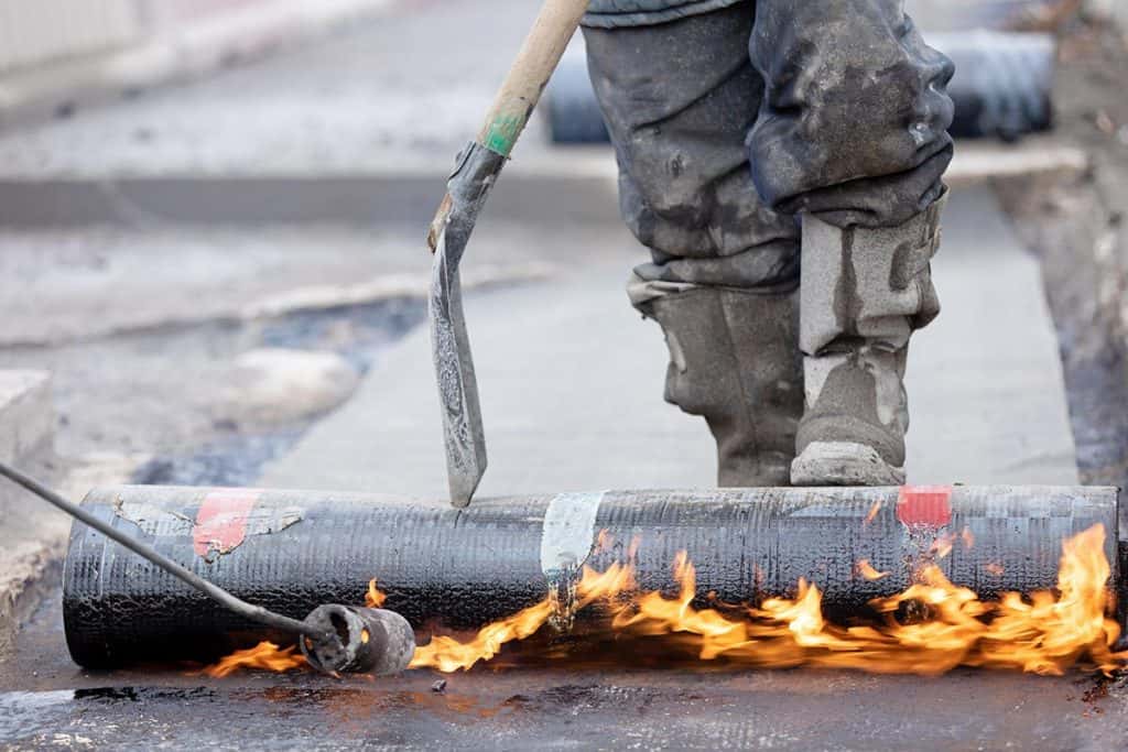 Construction worker applying SBS modified bitumen roll sheet over a concrete bridge deck with butane gas bow torch