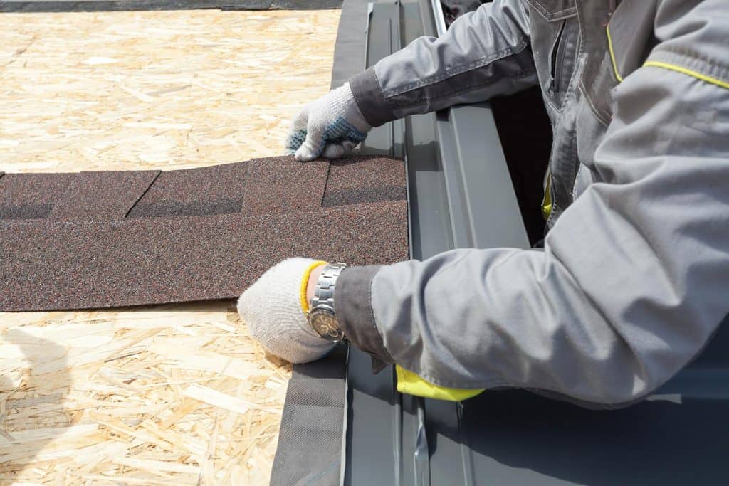 Professional roofer worker lays asphalt sheet on the rooftop
