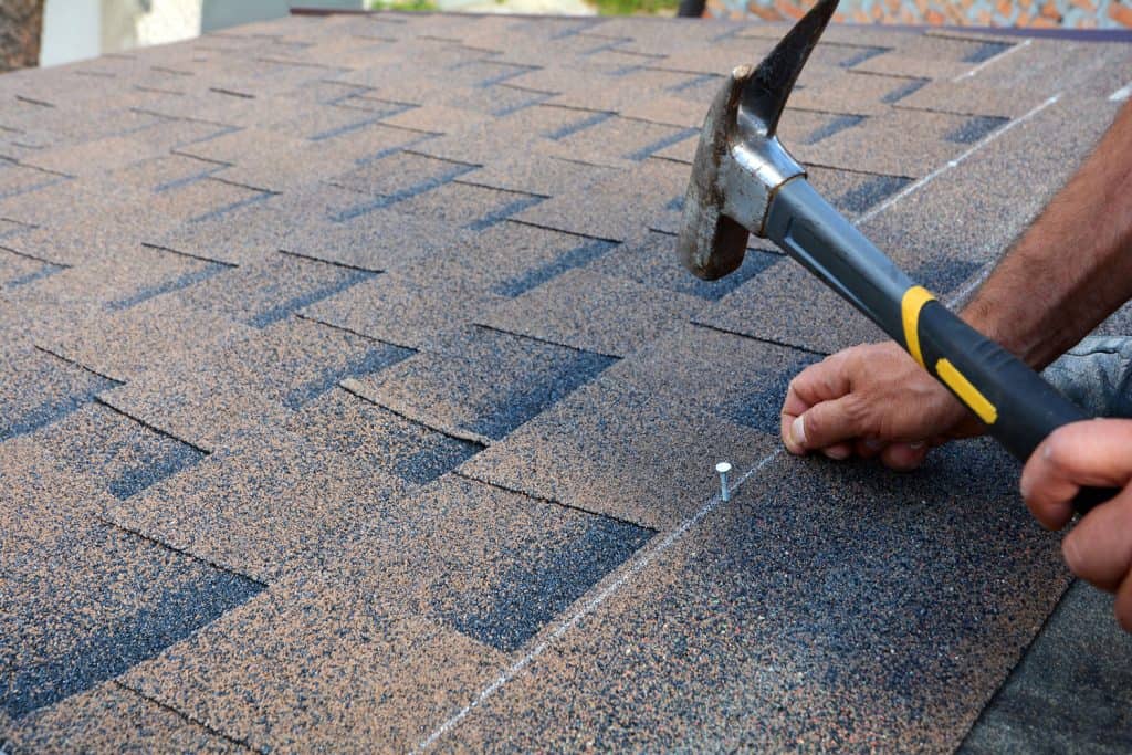 Roof installer using a hammer to install asphalt shingle
