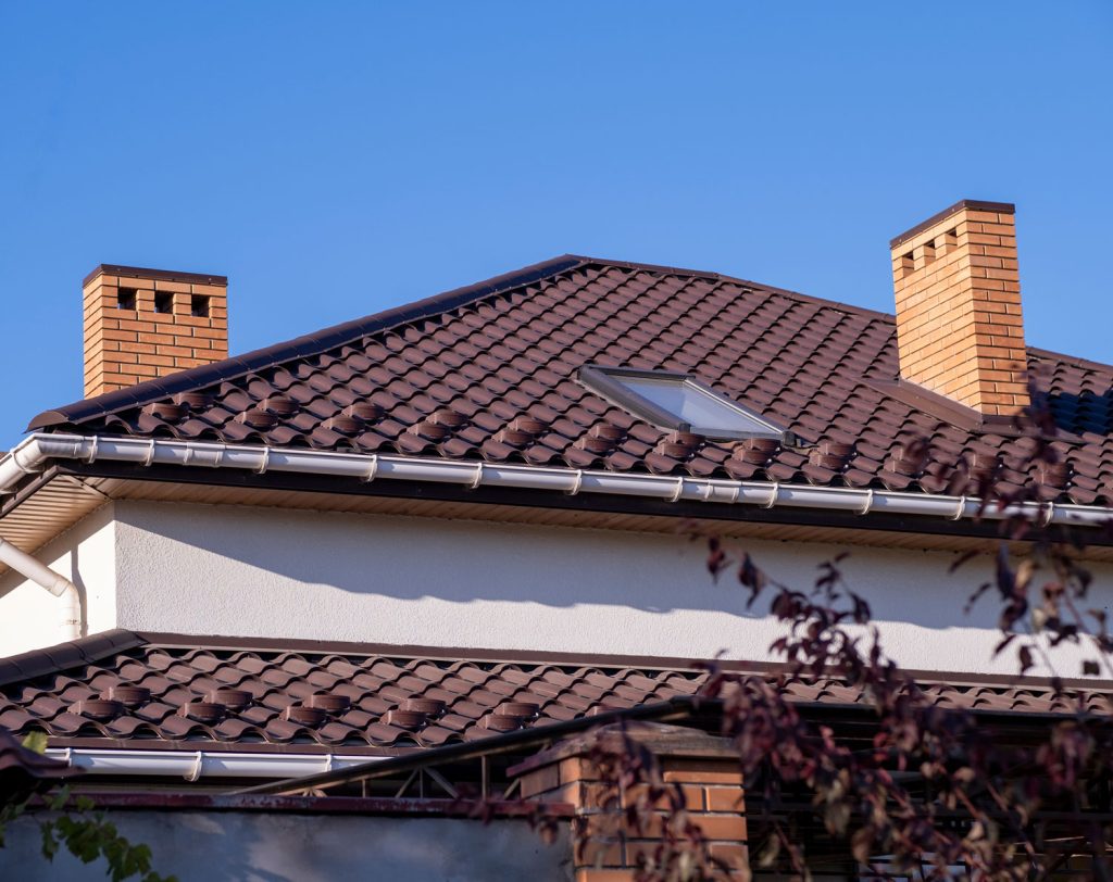 Roof with brown metal tiles and a dormer window. There are snow holders on the roof.
