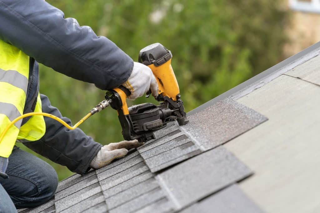 Roofer using a brad nail gun to install asphalt shingle roofing