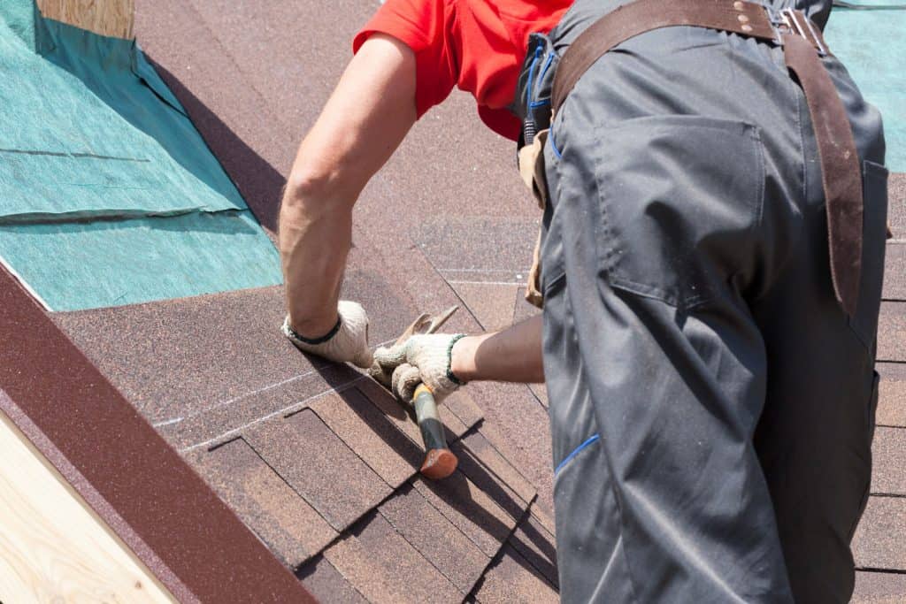 Roofer using a hammer to install red asphalt shingles