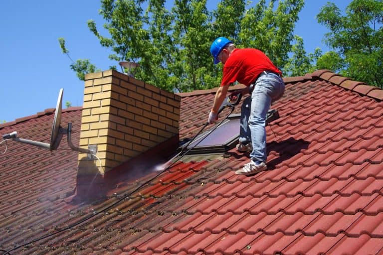 A worker on top of building washing tile with professional equipment, How To Clean Roof Tiles?