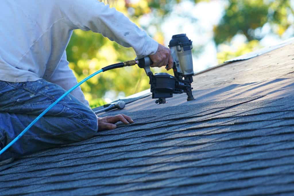 Worker using a pneumatic brad nailer to install asphalt shingle roofing