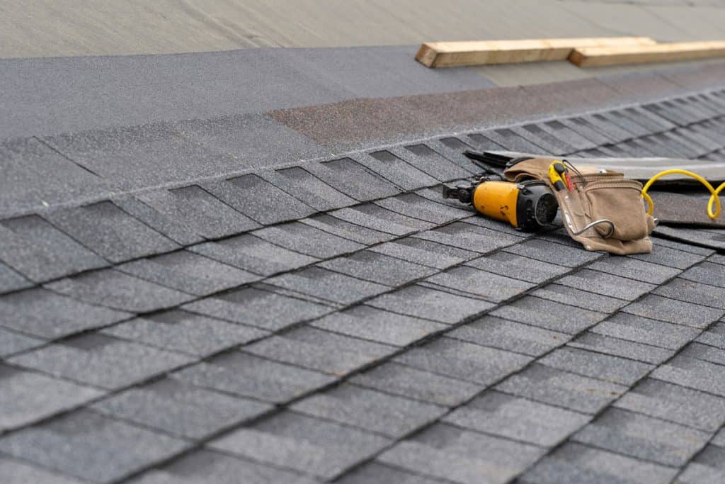 tooltoolbelt with instrument and nail gun lying on asphalt or bitumen shingle on top of the new roof under construction residential house orbelt with instrument and nail gun lying on asphalt or bitumen shingle on top of the new roof under construction residential house