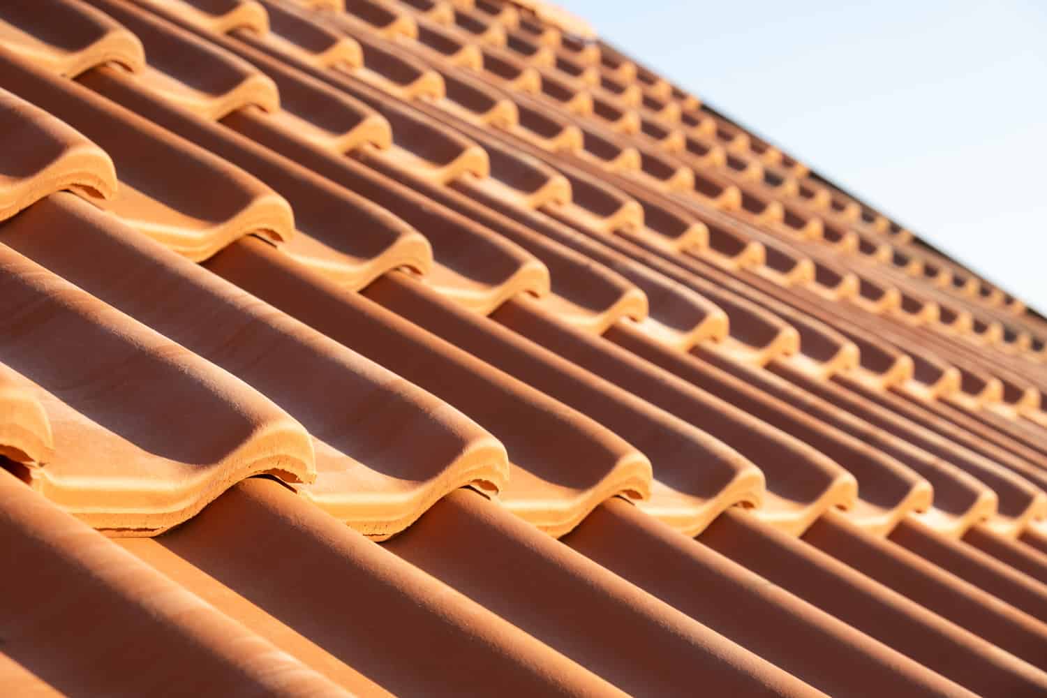 Overlapping rows of yellow ceramic roofing tiles covering residential building roof.
