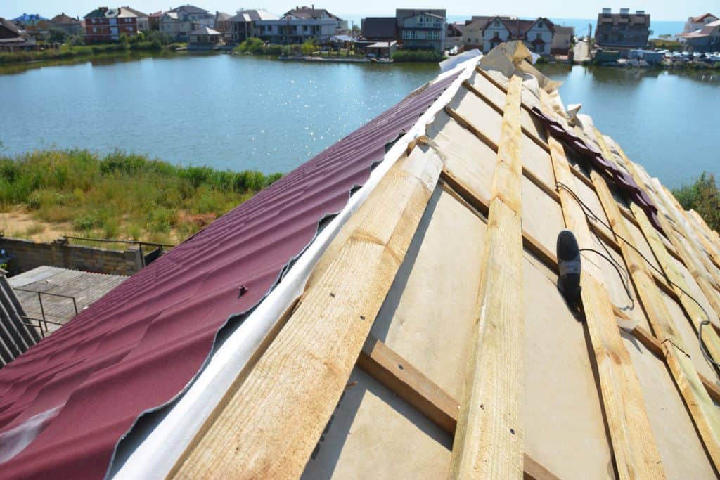 A close-up on an unfinished roof ridge with a vapor, moisture barrier, and Lightweight Metal Roofing Sheets installed over a roofing deck, sheathing.