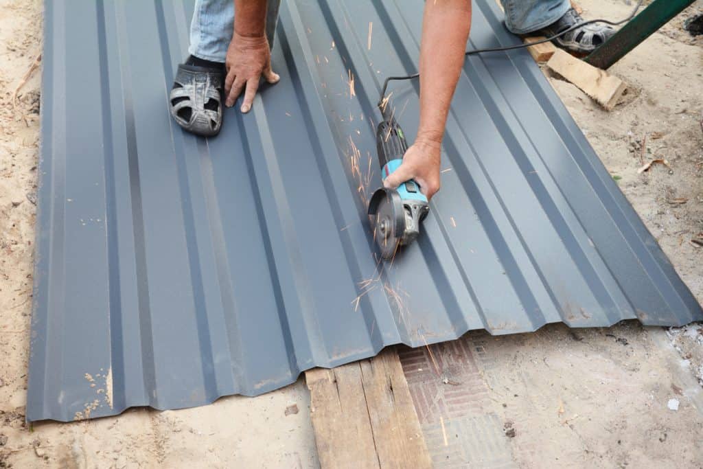 A building contractor is cutting corrugated metal roof sheet using an angle grinder to cover the rooftop of the house construction.