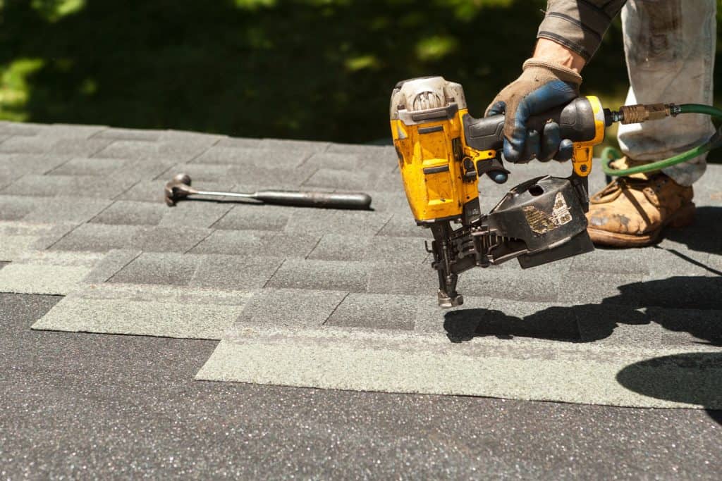 Roofers replacing old roof shingles with New shingles on residential home using a nail gun.

