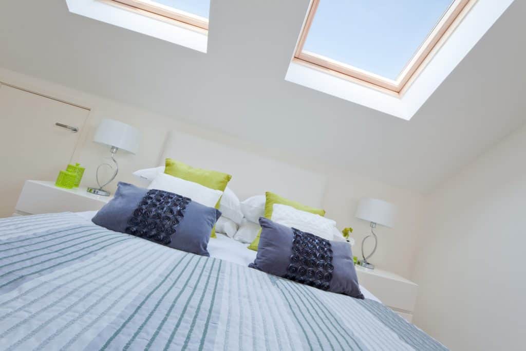 Stylish modern loft bedroom with rooflights and bed dressed with brightly coloured fashionable fabrics
